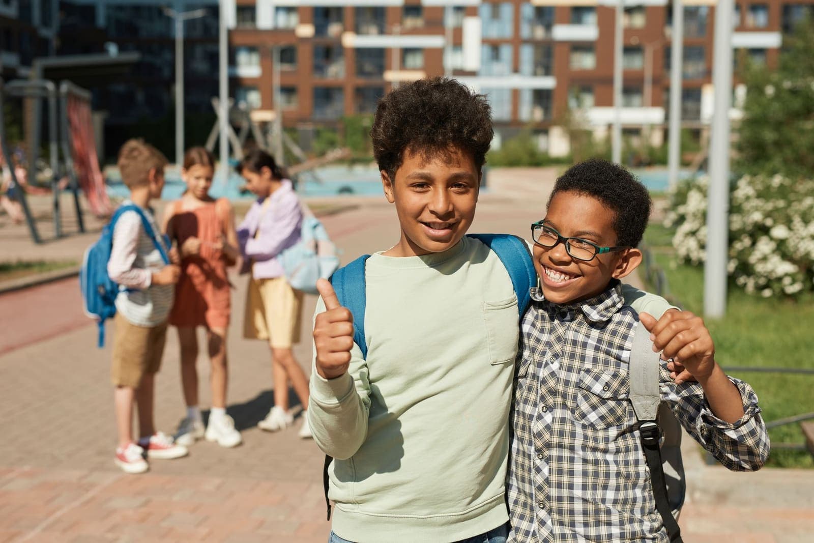 Two pupils with school backpacks smiling and giving a thumbs up