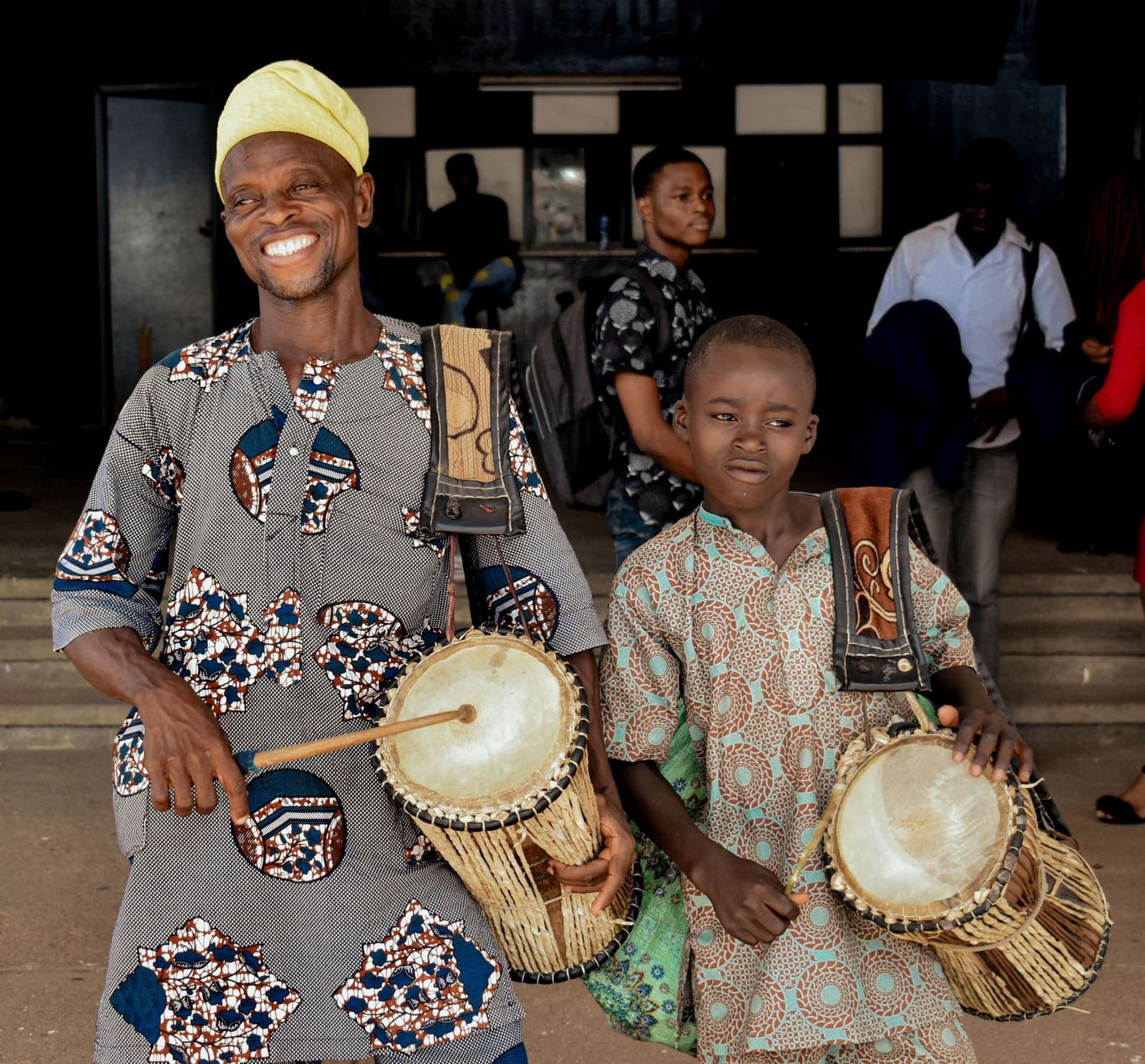 A child learning to play traditional drums alongside a musician