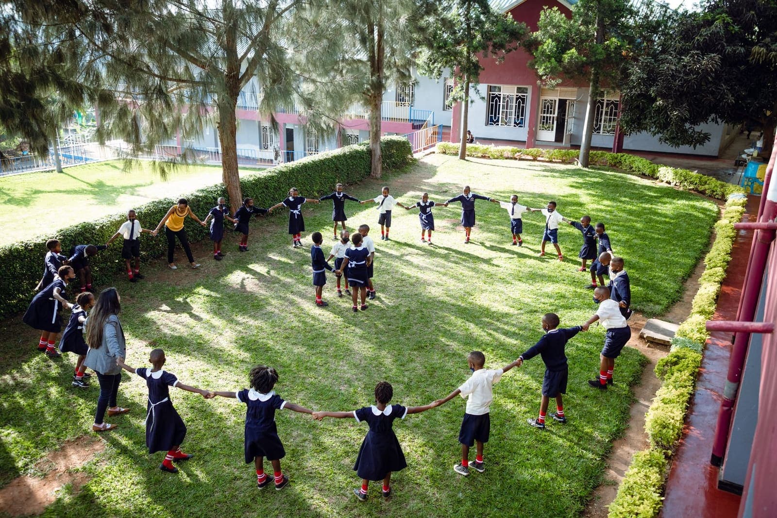 Children holding hands in a circle on a green school lawn