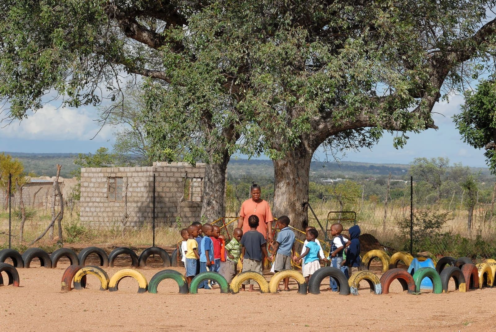 Children playing together in an outdoor school playground shaded by a large tree