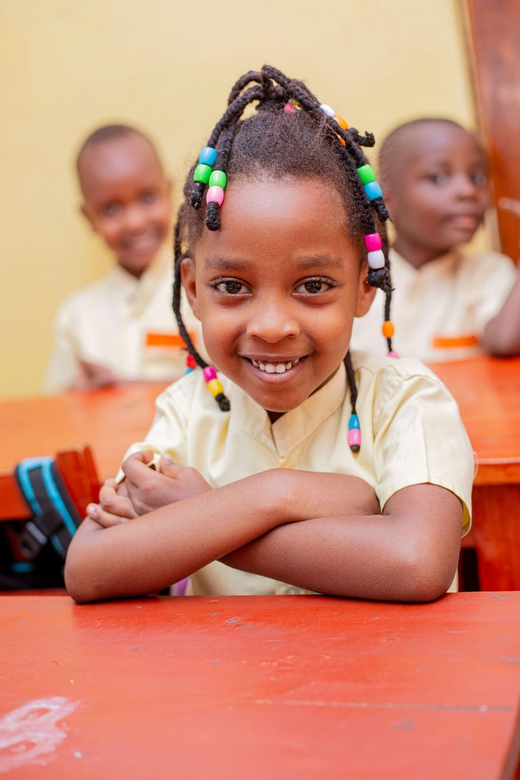 A smiling primary school pupil resting on her desk in a bright classroom