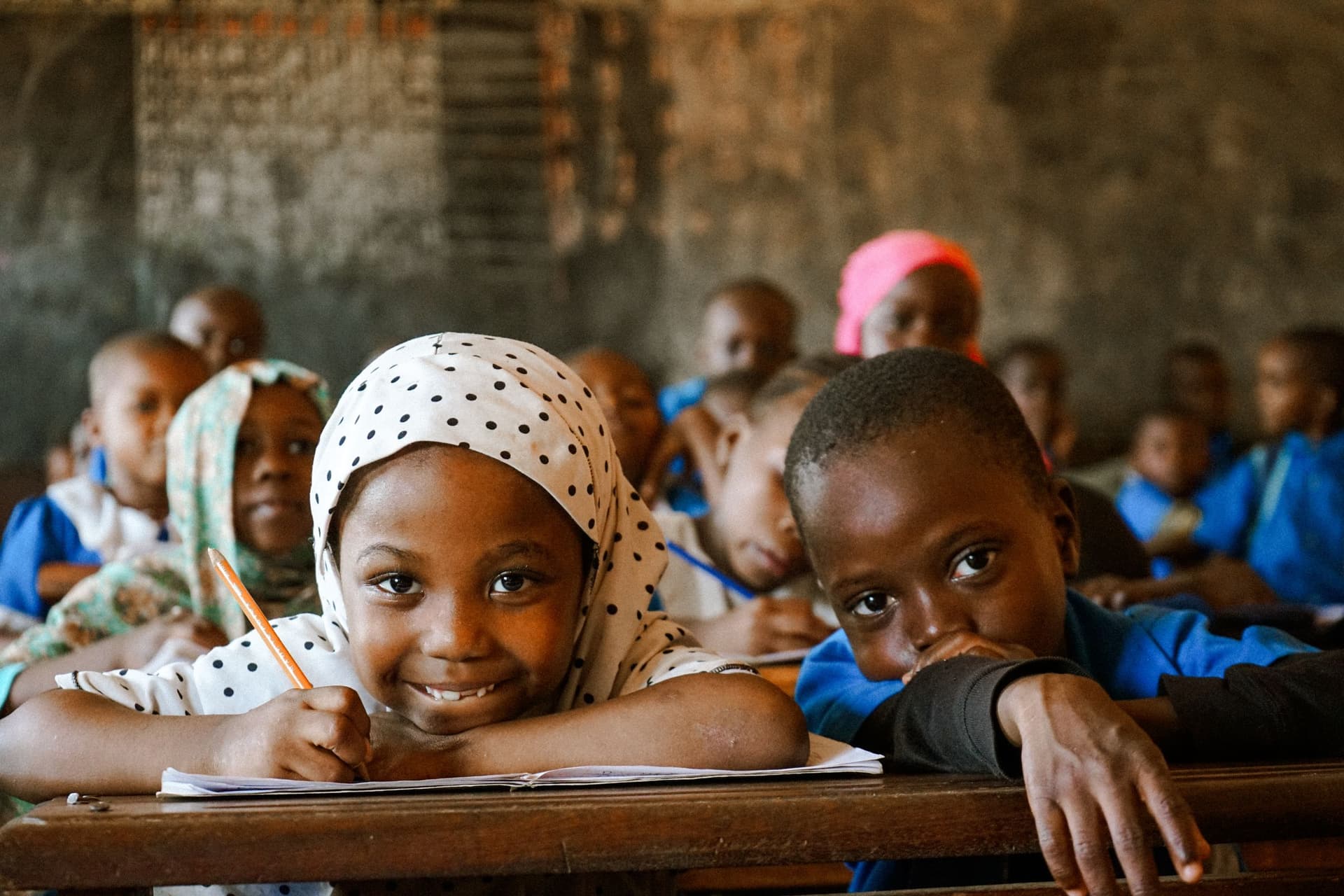 A joyful pupil smiling while writing at her desk in class